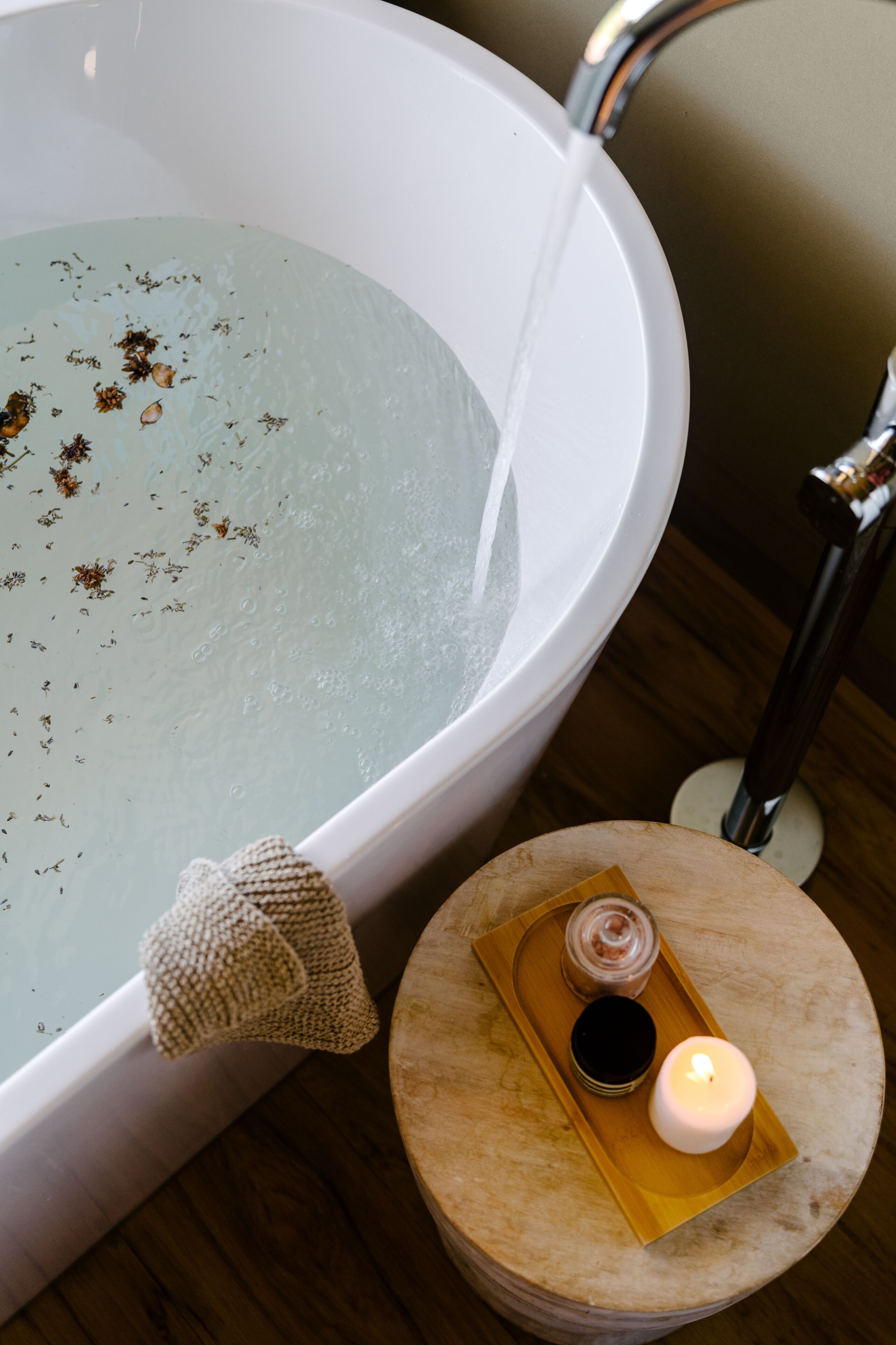 A bathtub with water, a towel, a candle, and a tray with a jar and a candle.