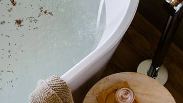 A bathtub with water, a towel, a candle, and a tray with a jar and a candle.