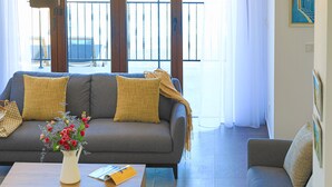 A living room with a grey sofa, two yellow cushions, a white vase with red flowers, and a wooden coffee table. - Villa Salina: Modern Holiday Villa, Private Pool, Views, WiFi, A/C (Meladeia)