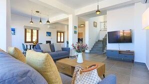 A spacious living room with a sofa, coffee table, and TV. There is a staircase leading to another level. - Villa Salina: Modern Holiday Villa, Private Pool, Views, WiFi, A/C (Meladeia)