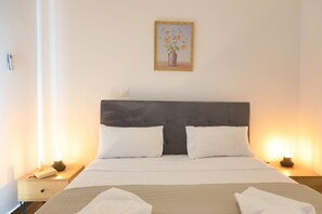 Una cama bien tendida con sábanas blancas, dos almohadas y una mesita de noche con una lámpara y un control remoto.