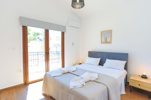 Un dormitorio con cama, mesita de noche, lámpara, un cuadro y una puerta corredera de cristal que da a un espacio exterior.