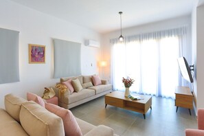 Una sala de estar moderna con un sofá color beige, una mesa de centro de madera y un televisor sobre un mueble.