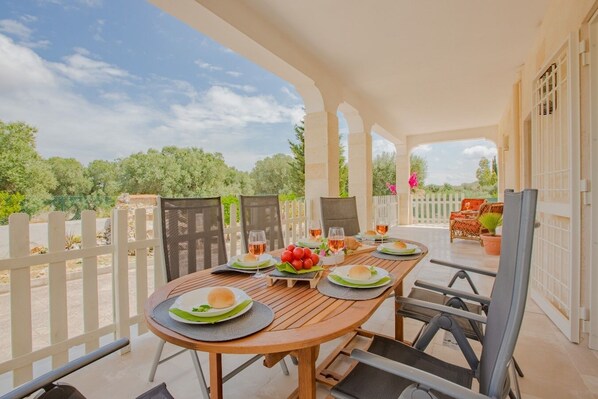 An outdoor dining area with a wooden table, chairs, and a white picket fence.
