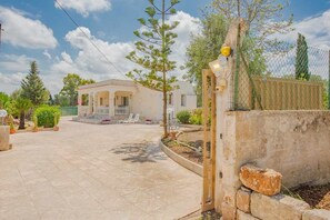 A spacious courtyard with a white building, a stone wall, and a gate.