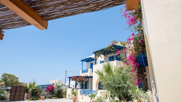 En byggnad i medelhavsstil med en träpergola, färgstarka bougainvilleablommor och en klarblå himmel.