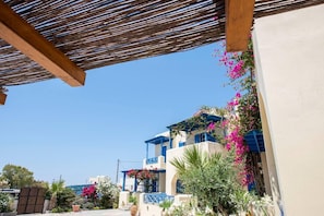 A Mediterranean-style building with a wooden pergola, vibrant bougainvillea flowers, and a clear blue sky.