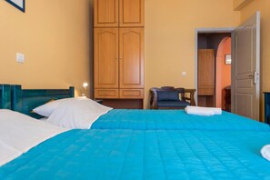 A hotel room with two beds, wooden wardrobes, a chair, and a door leading to another room.