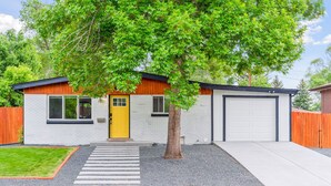 A modern single-story house with a yellow front door, a garage, and a tree in the front yard. - Modern Family Oasis ~ 5★ Location, Games, Backyard (Arvada)