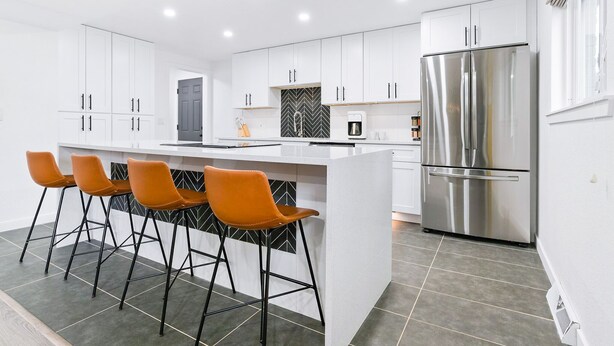 A modern kitchen with white cabinets, a stainless steel refrigerator, and a central island with bar stools. - Modern Family Oasis ~ 5★ Location, Games, Backyard (Arvada)