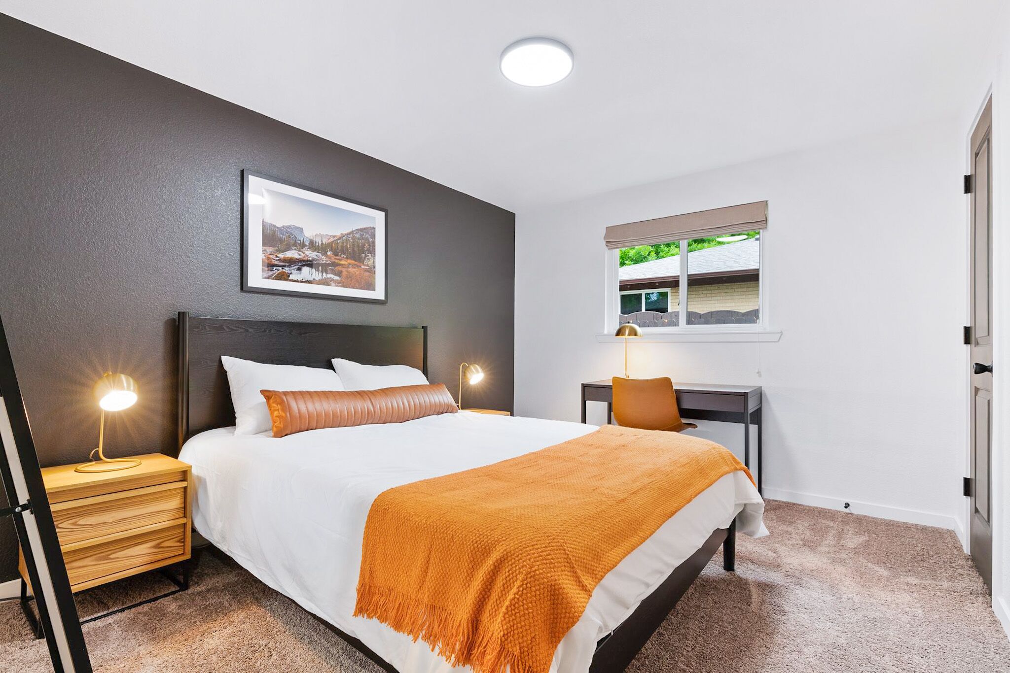 Une chambre à coucher avec un lit, des tables de chevet, un bureau et une fenêtre.
