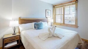 A hotel room with a large bed, two bedside lamps, a nightstand, a window with a wooden frame, and a framed picture on the wall. - 1 Bedroom Mountain Condo in River Run Village With Expansive Mountain Views and Walking Distance to Ski Slopes (Keystone)