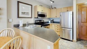 A modern kitchen with wooden cabinets, stainless steel appliances, a large island, and a framed picture on the wall. - 1 Bedroom Mountain Condo in River Run Village With Expansive Mountain Views and Walking Distance to Ski Slopes (Keystone)