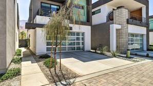 A modern two-story building with a garage, a balcony, and a small garden area with a tree. - Mid-Century Modern Palm Springs Home w/ Pool (Palm Springs)