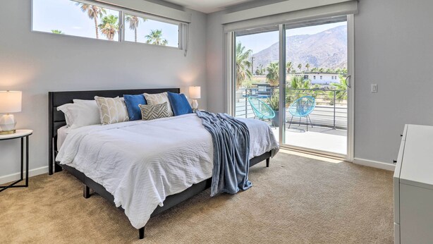 A bedroom with a bed, a ceiling fan, a nightstand, a lamp, and a view of the outdoors through a sliding glass door. - Mid-Century Modern Palm Springs Home w/ Pool (Palm Springs)