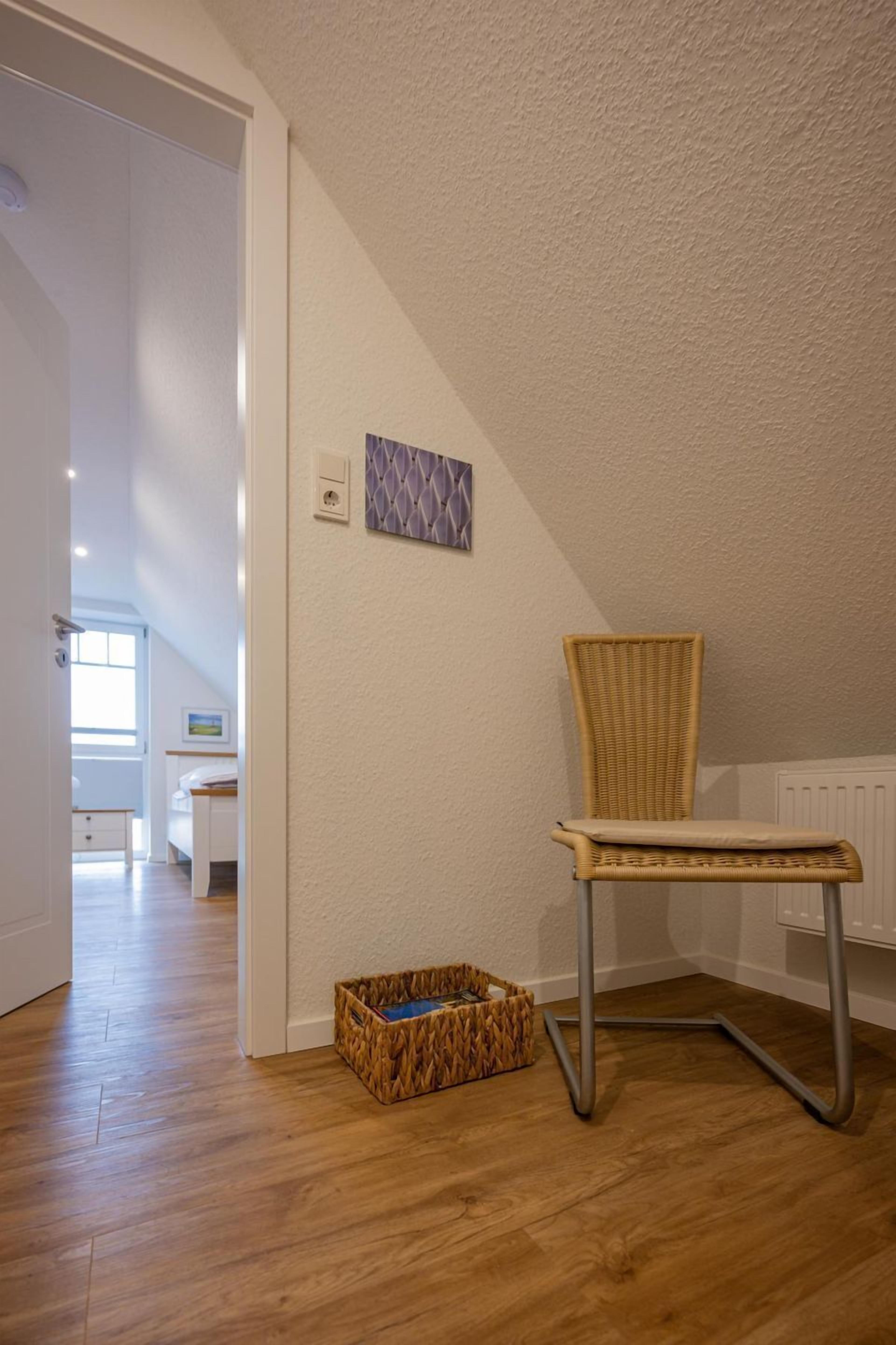 A room with a wooden floor, a wicker chair, a small woven basket, and a radiator.