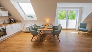 A modern kitchen with a skylight, a dining area with a table and chairs, and a view of greenery outside. - Wattperle - Wunderschöne Obergeschosswohnung in Greetsiel (Krummhörn)