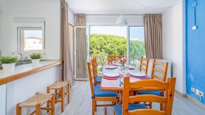 Comedor con mesa dispuesta para seis comensales, sillas de madera, barra con taburetes y vistas a zonas verdes a través de amplios ventanales.