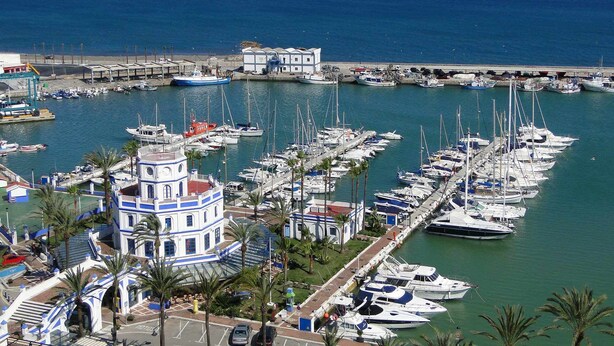 A marina with numerous boats docked, a prominent building with a tower, and a clear view of the sea. - Modern one  km from the centre and La Rada Beach. (Estepona)