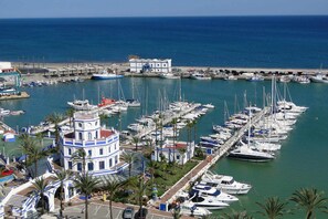 A marina with numerous boats docked, a prominent building with a tower, and a clear view of the sea. - Modern one  km from the centre and La Rada Beach. (Estepona)