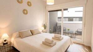 A bedroom with a bed, two bedside lamps, a small table with a lamp, and a balcony with chairs and a table. - Modern one  km from the centre and La Rada Beach. (Estepona)