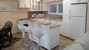 Een moderne keuken met witte kasten, een centraal eiland met barstoelen, een ingebouwde magnetron en een koelkast.
