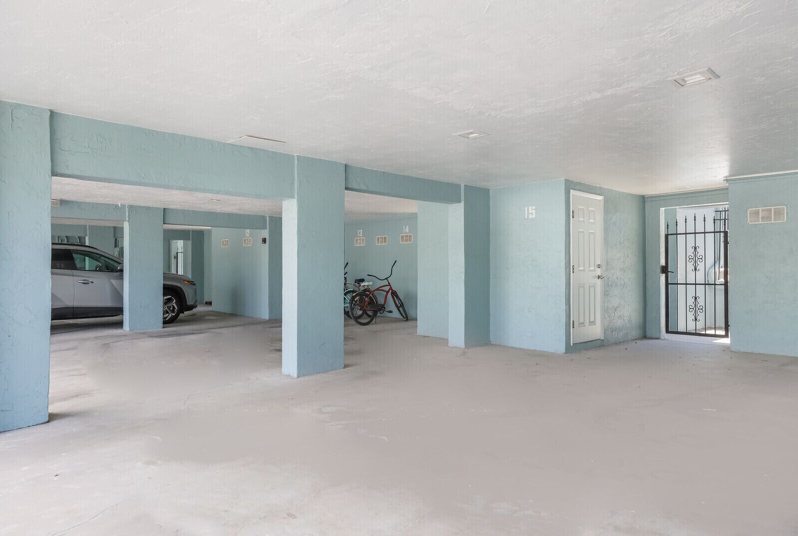 Un aparcamiento con paredes azul claro, plazas numeradas y una bicicleta estacionada en una de ellas.
