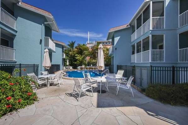A pool area with lounge chairs and umbrellas, surrounded by multi-story buildings with balconies.