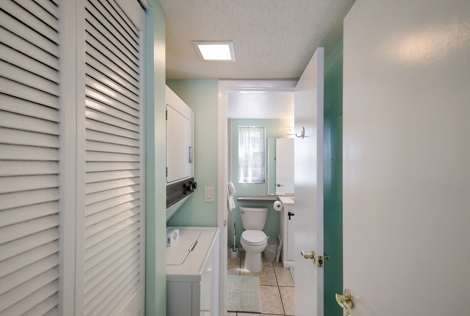 Un estrecho pasillo que conduce a un baño con inodoro, lavamanos y ventana.