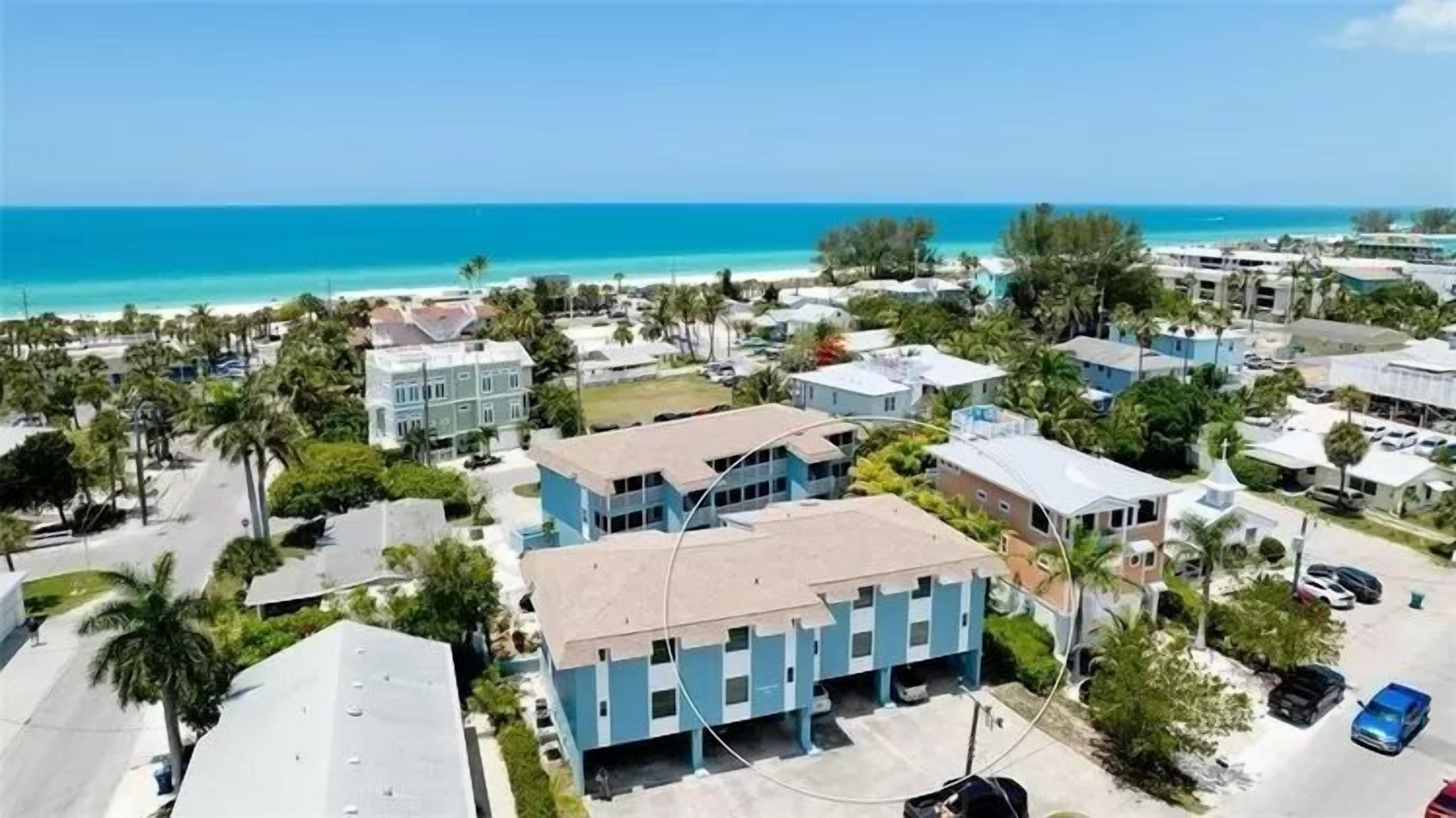 A coastal residential area with multiple two-story houses, a clear view of the ocean, and a parking area with cars.