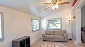 A living room with a ceiling fan, a beige sofa, a floor lamp, and a bookshelf. - Cozy little Home in Quiet neighborhood Off of major road (Port Charlotte)