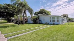 A single-story house with a front yard, a palm tree, and a clear sky. - Cozy little Home in Quiet neighborhood Off of major road (Port Charlotte)