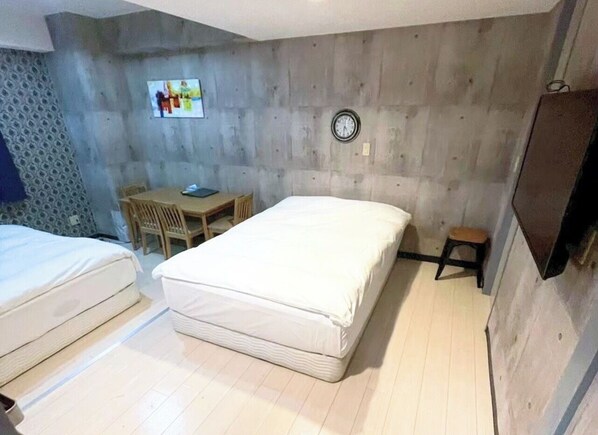 A bedroom with two beds, a desk, a chair, a clock, and a television.