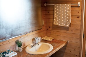 A wooden bathroom with a sink, a towel rack with a polka dot towel, a small plant, and a cup. - Villa Regalo (Beppu)