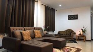 A living room with a sectional sofa, a patterned armchair, a small side table with a lamp, and a decorative rug.