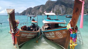 Two traditional boats docked at a beach with clear turquoise water and mountainous background.