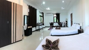 A hotel room with two beds, a wardrobe, a desk with a chair, a small table with a vase, and a window with curtains.