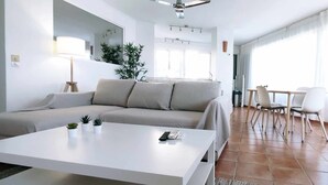 Ett modernt vardagsrum med en beige soffa, ett vitt soffbord och en matplats med vita stolar och ett bord.