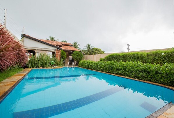 A rectangular swimming pool with tiled edges, surrounded by a low hedge and a brick wall.