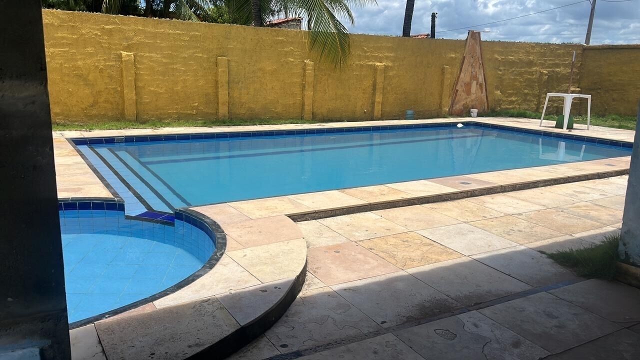 Una piscina rettangolare con bordo piastrellato, circondata da un solarium piastrellato e un muro giallo.