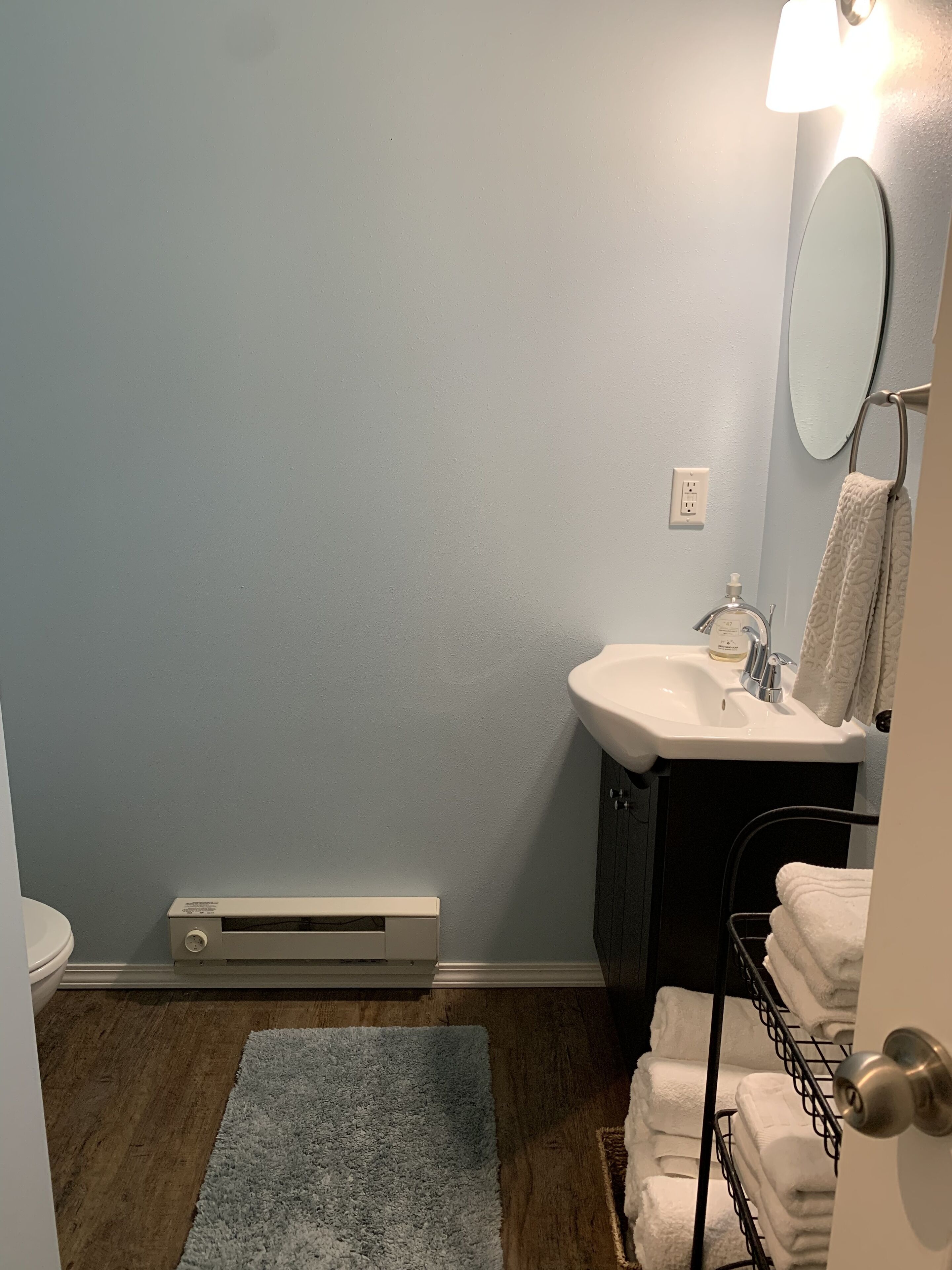 A bathroom with a white sink, a mirror, a towel rack, and a heater on the floor.