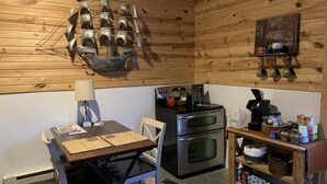A cozy kitchen with wooden walls, a dining table with chairs, a coffee machine, and a shelf with kitchenware. - Salt and Light Retreat for Overnight Stays in Rural South Dakota (Hayti)