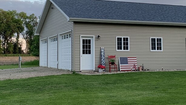 A single-story building with a garage, a welcome sign, and an American flag. - Salt and Light Retreat for Overnight Stays in Rural South Dakota (Hayti)