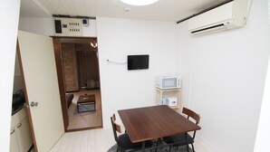 Habitació compacta amb taula de dinar de fusta, dues cadires, televisor penjat a la paret i microones damunt d'una estantàlia.