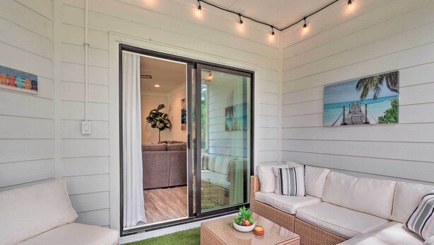 Una sala moderna con un ventanal que da a un balcón, un conjunto de sofás, una mesa de centro con frutas y un cuadro de una playa.