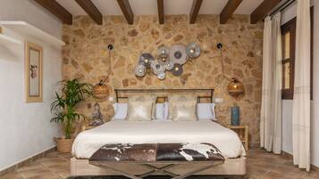 Une chambre avec un mur en pierre, un lit avec une tête de lit, une plante en pot et une table de chevet.
