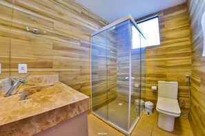 Un baño moderno con diseño de pared de madera, cabina de ducha de vidrio, lavamanos de mármol y un inodoro.