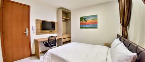 Una habitación de hotel con cama, escritorio, silla, televisor y un cuadro en la pared.