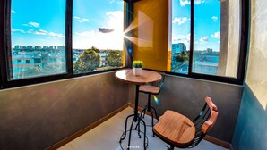 Un balcón con vistas a un paisaje urbano, una mesa redonda con una planta en maceta y una silla de madera.