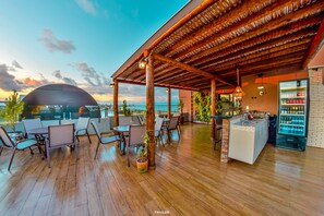An outdoor seating area with wooden flooring, tables, chairs, and a bar area with a refrigerator. - Hotel Aracaju suítes (Aracaju)